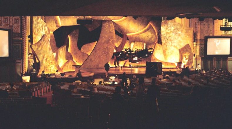 Shot taken from the back of the Emmys venue that shows the stage golden lit preparing for the long night.