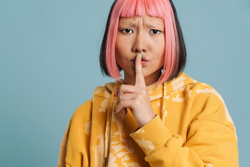 Asian girl with pink hair and piercing showing silence gesture