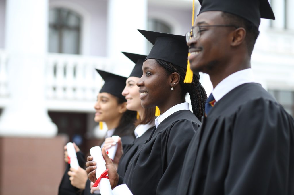 Portrait of happy multiracial graduates in gowns holding diplomas outdoors, education