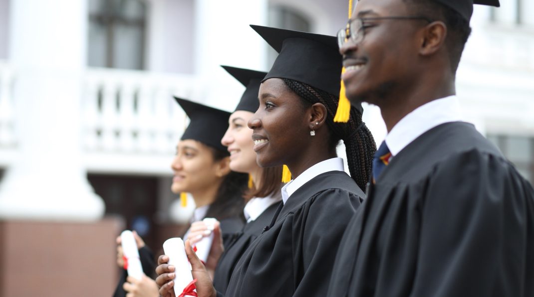 Portrait of happy multiracial graduates in gowns holding diplomas outdoors, education