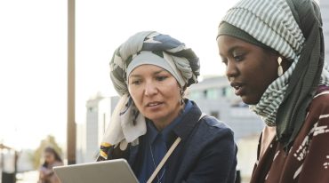 Two refugee women using tablet (Photo via Envato Elements)