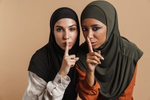 Young muslim women in hijab showing silence gesture at camera