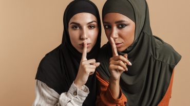 Young muslim women in hijab showing silence gesture at camera